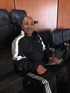 Johnny W. is sitting in a large leather chair in a box suite during the Orlando Magic basketball game.
