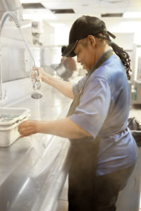 Woman using long kitchen hose to clean dishes.