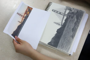 A boy sketches a very detail oriented picture of the Golden Gate bridge.