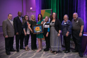 Group of people posing for a photo after accepting thier framed award.
